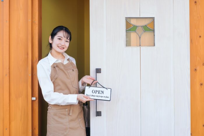 カフェ店舗の入口でOPENプレートを持つ女性スタッフ