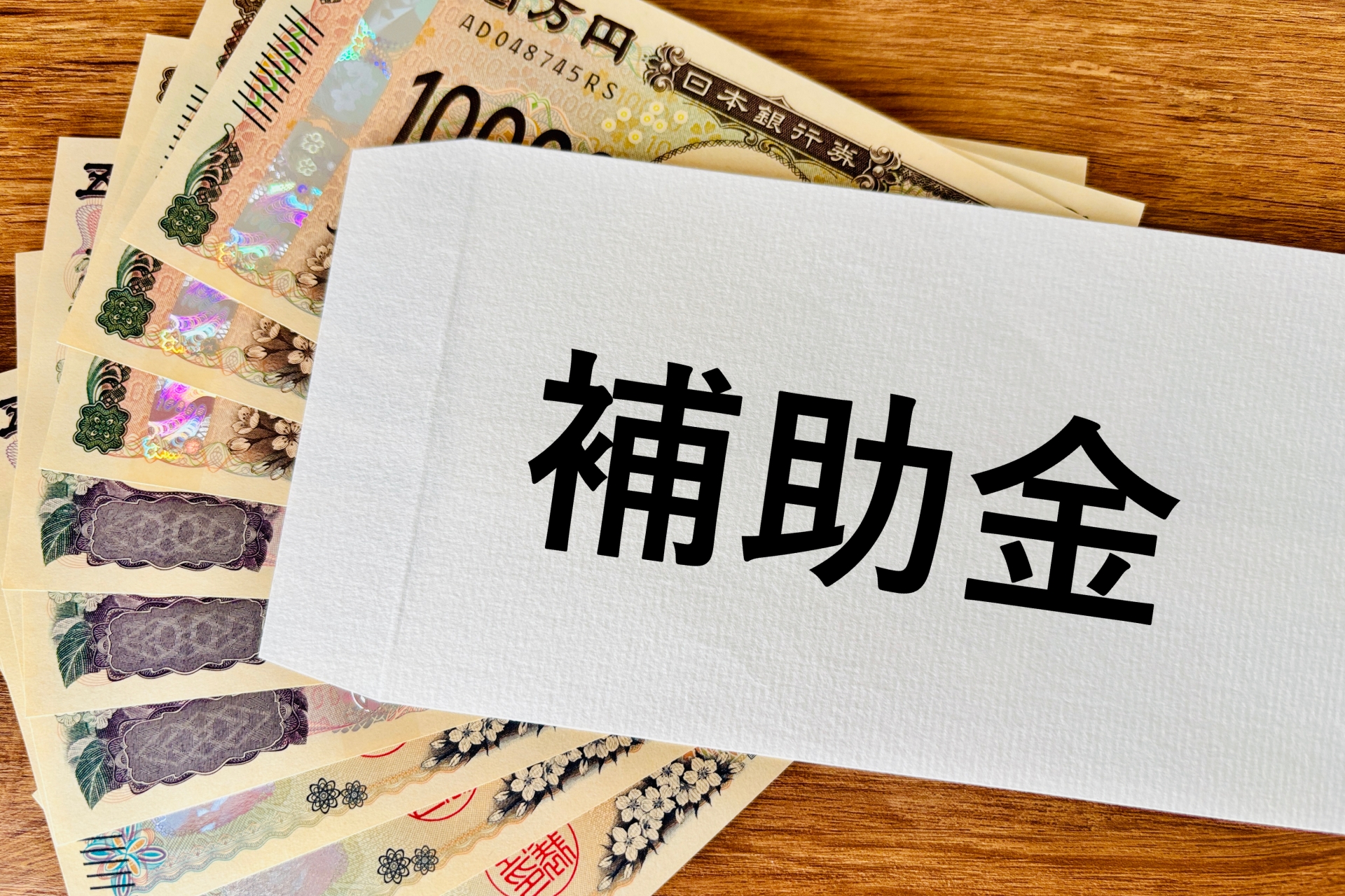 「補助金」と書かれた封筒と扇状に並べられた一万円札