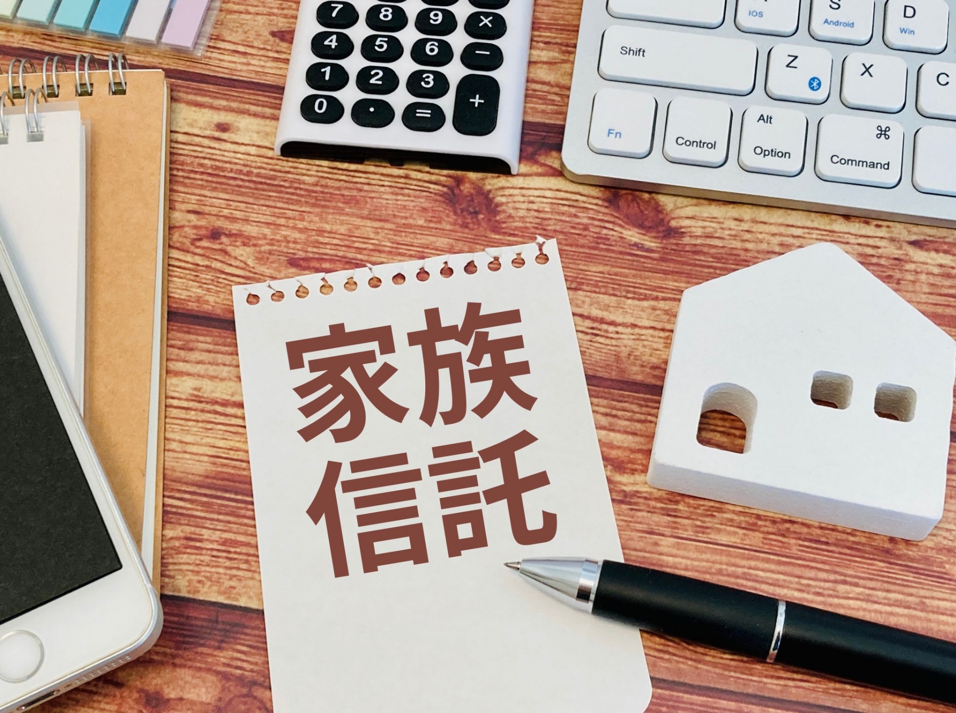 家族信託をイメージしたメモ帳と電卓・家の模型