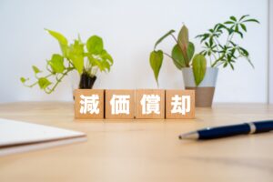 中古アパートの減価償却と節税効果を解説する「減価償却」のブロックとペン