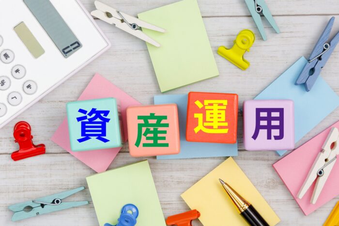 「資産運用」の文字ブロックと電卓・メモのイメージ。NISAで不動産投資信託を買うメリット・デメリットを整理する